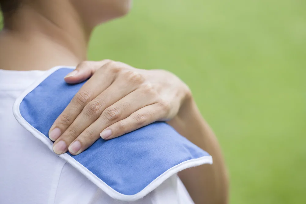 A woman applying a cold treatment with an ice pack on her shoulder.