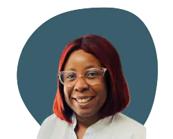 A woman at home with red hair and glasses smiling.