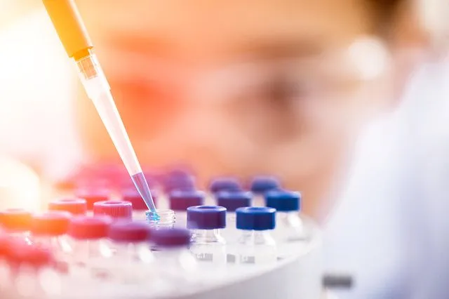 A scientist is performing services in a laboratory, holding a test tube in front of a microscope for lab testing