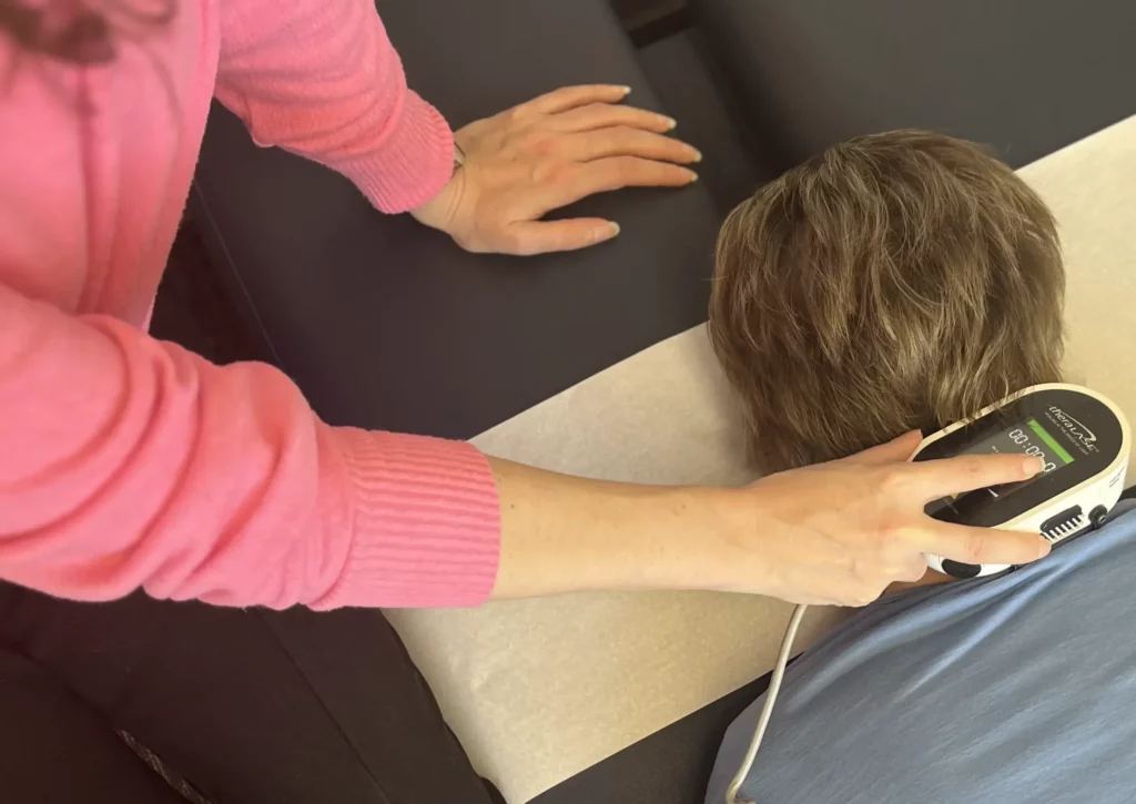 An osteopathic doctor providing services using an electronic device to adjust a patient's neck laser therapy.