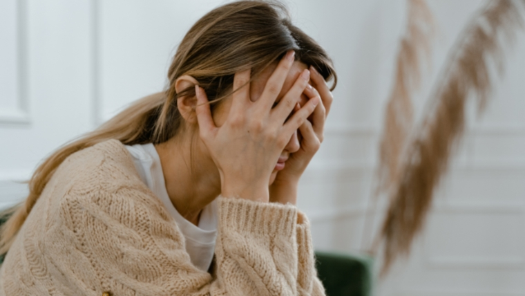 A stressed woman covering her face while sitting on a couch.