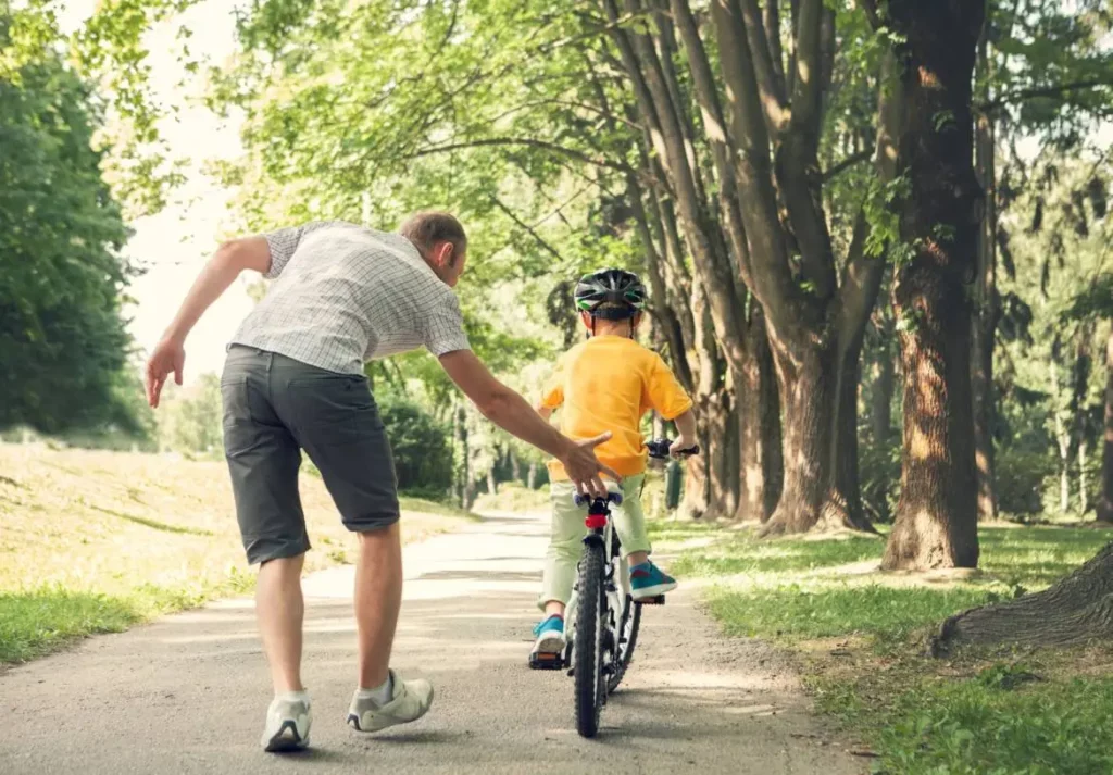 A man and a child having fun riding a bike in a park.