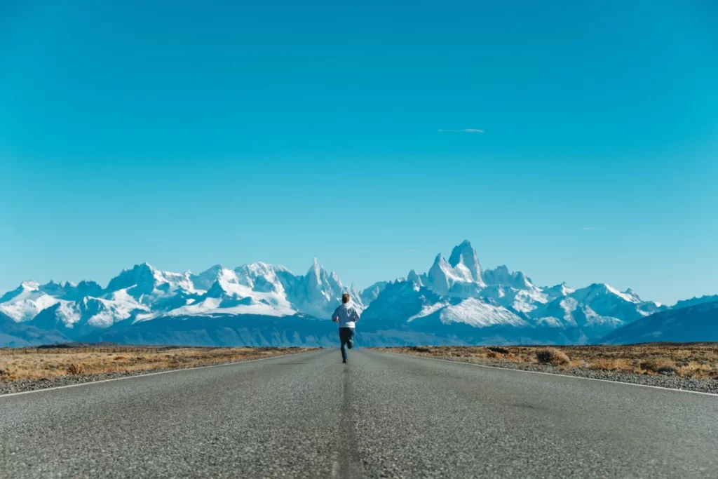A woman Hiking on an empty road with mountains in the background.