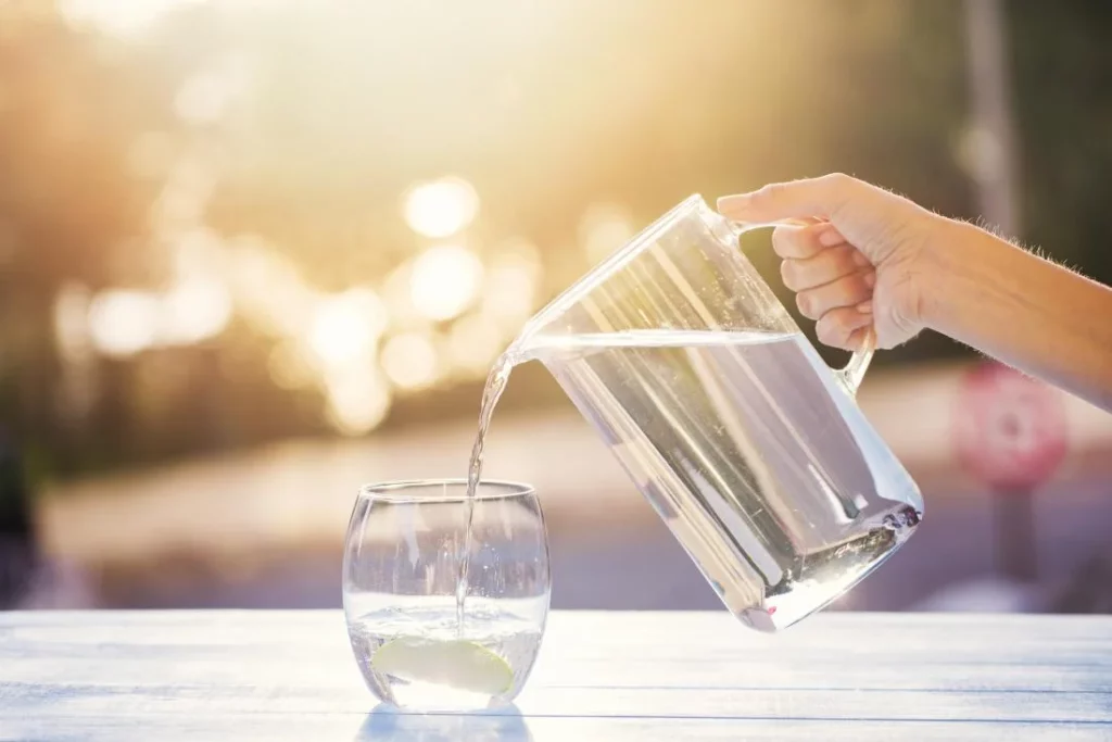 A person enjoying the benefits of drinking water by pouring it into a glass.