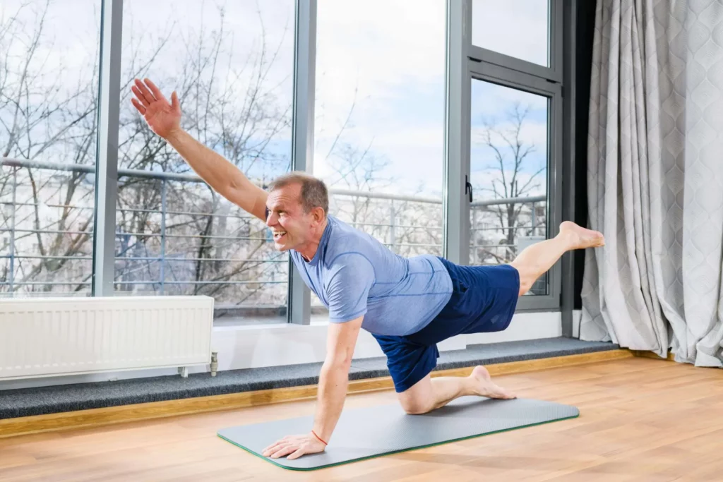 A man is doing yoga exercises for spinal stability in front of a window.