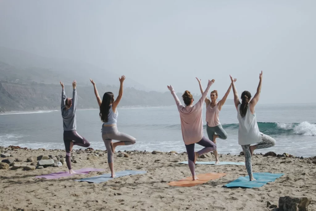 A group of women practicing yoga on the beach to get relaxation and peace.