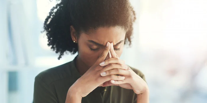 A black woman handling the stress of these tough times, with her hands on her face.