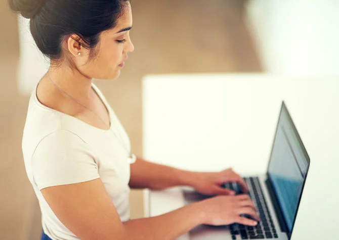 A woman with good posture working powerfully on a laptop in front of a white table.