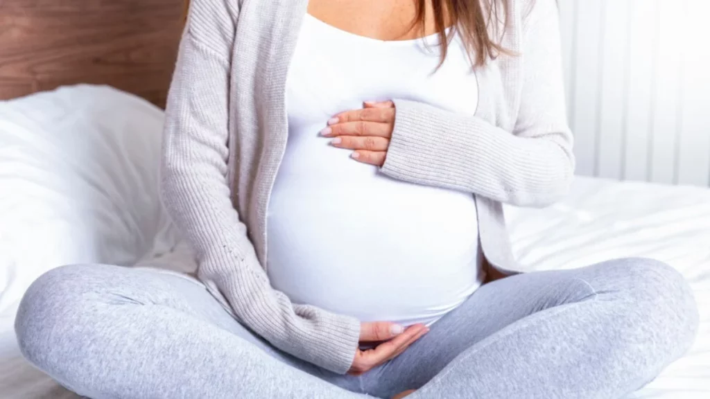 A safe pregnant woman sitting on a bed.